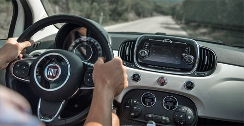 Car rental in Olbia: close-up of a driver's hands on the steering wheel of a modern Fiat 500 while traveling through the Sardinian countryside