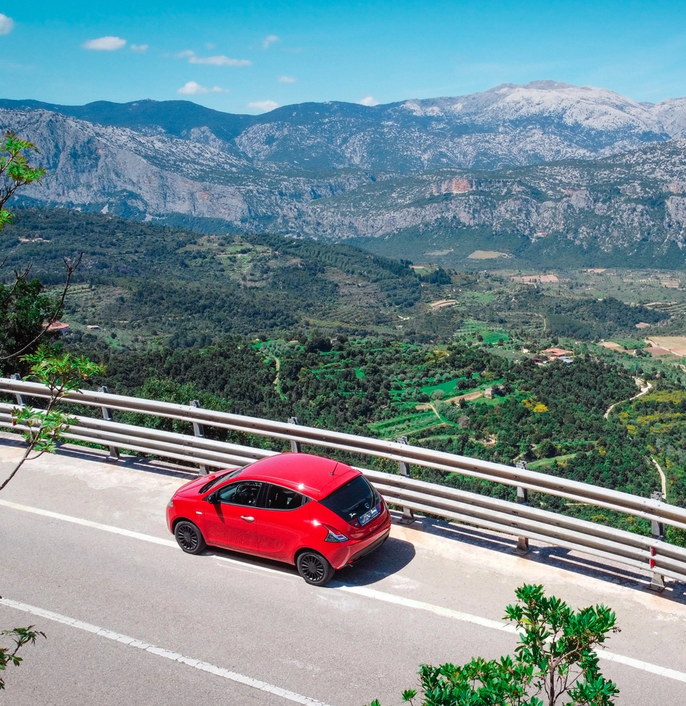 Lancia Ypsilon rossa Only Sardinia Autonoleggio su una strada panoramica tra le montagne della Sardegna.
